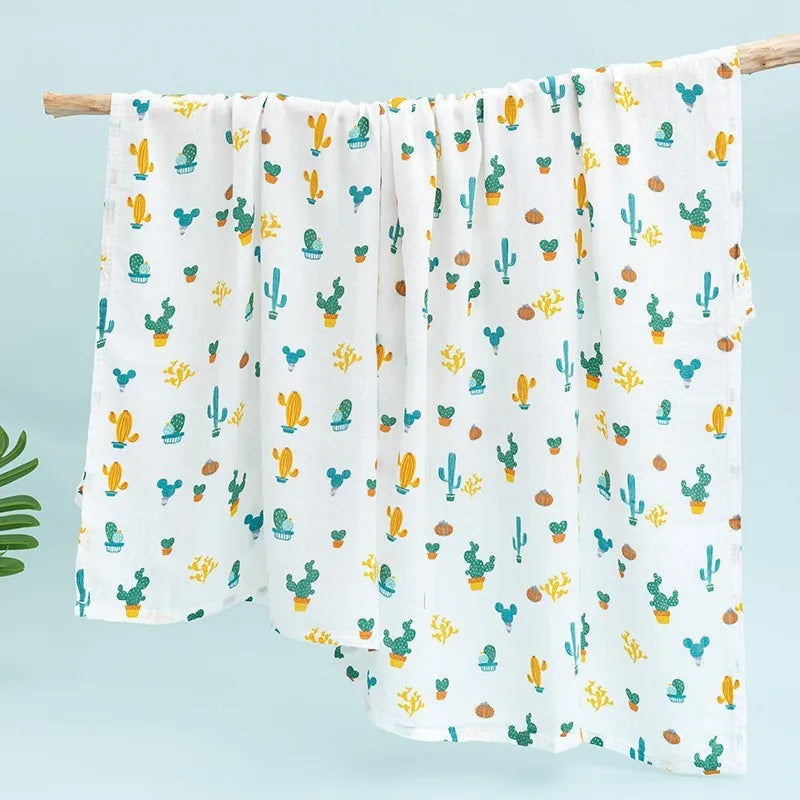 White muslin swaddle blanket with a repeating pattern of colorful cacti and succulents hanging on a wooden rod.