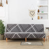 A gray geometric print spandex slipcover on a sofa bed with a white accent, displayed in a bright room.