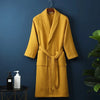 A mustard yellow cotton terry robe hanging on a dark blue wall.