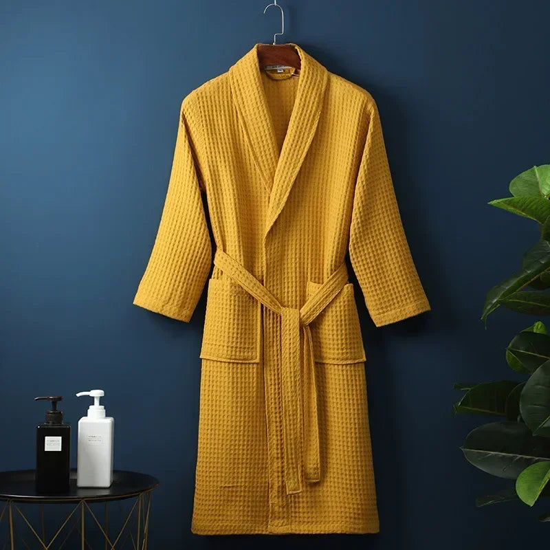 A mustard yellow cotton terry robe hanging on a dark blue wall.