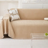 A beige chenille sofa cover draped over a sofa with a patterned throw pillow and a glass table.
