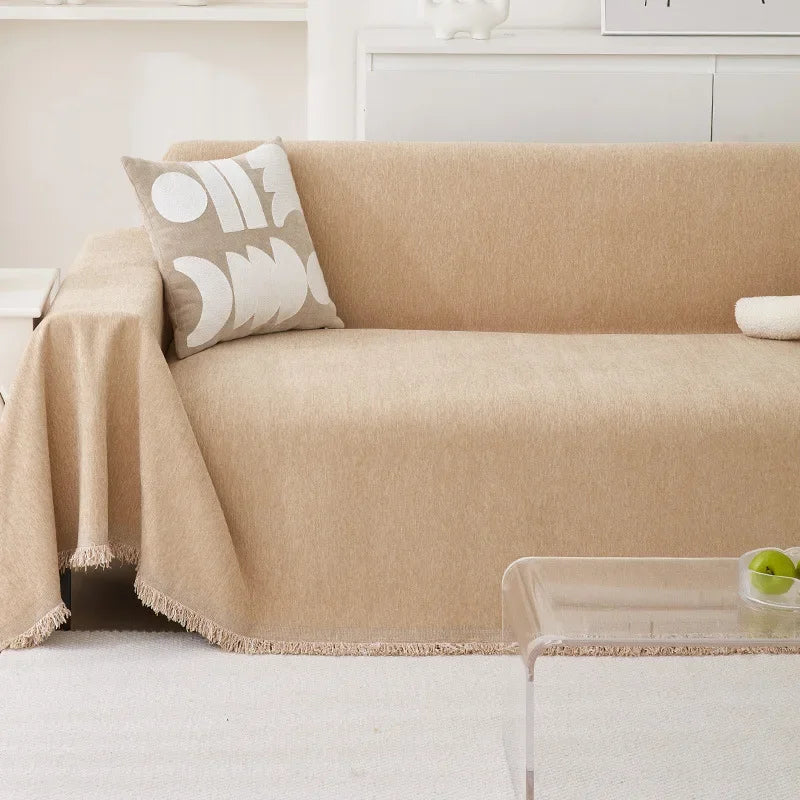 A beige chenille sofa cover draped over a sofa with a patterned throw pillow and a glass table.