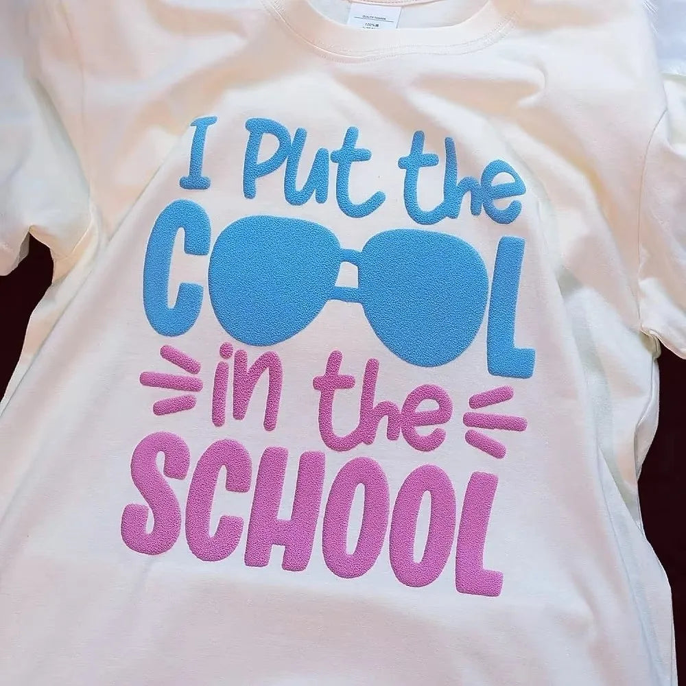 A light pink t-shirt features a blue graphic text that reads I Put the COOL in the SCHOOL