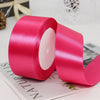 Roll of bright pink satin craft ribbon with white filling on a white background.