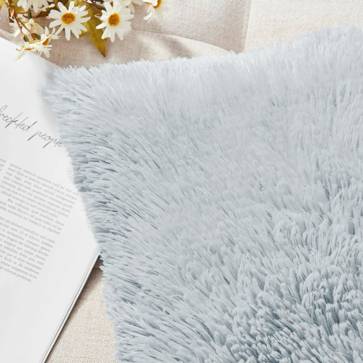 A light blue faux fur throw blanket draped next to a white paper with text and some dried flowers.