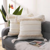A white boho tufted throw pillow cover with beige tassels resting on a gray sofa.