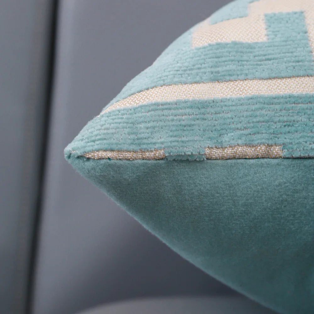 A close-up of a teal geometric jacquard lumbar pillow cover with light blue stripes.