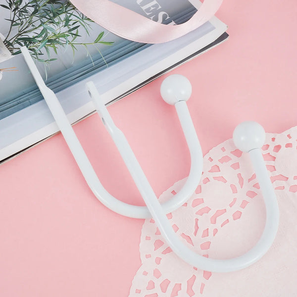 A set of two white retro metal curtain holdback hooks displayed on a pink background.