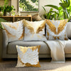 Decorative throw pillow covers featuring golden accents and white feather wings on a neutral sofa.