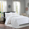 White embroidered bedding set with sheer curtains and natural light in a bedroom setting.