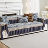 A gray quilted sofa cover with blue and gold patterned fabric and decorative trim on a white sofa.