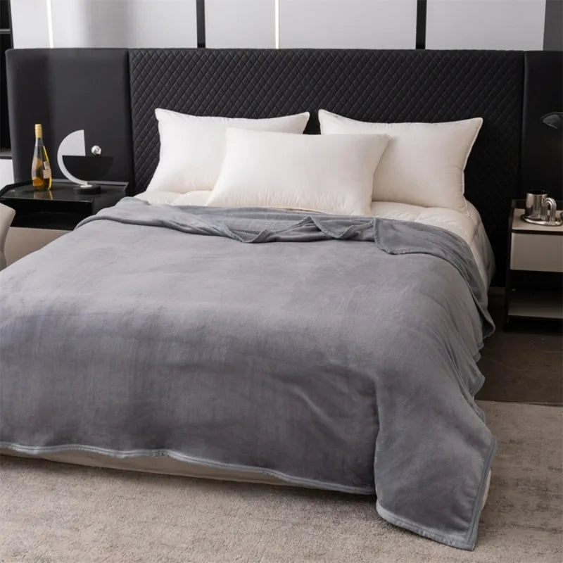 A gray flannel throw blanket is draped over a bed with white pillows and dark bedding.