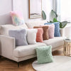A collection of fluffy velvet throw pillows in pastel and muted tones arranged on a white sofa.
