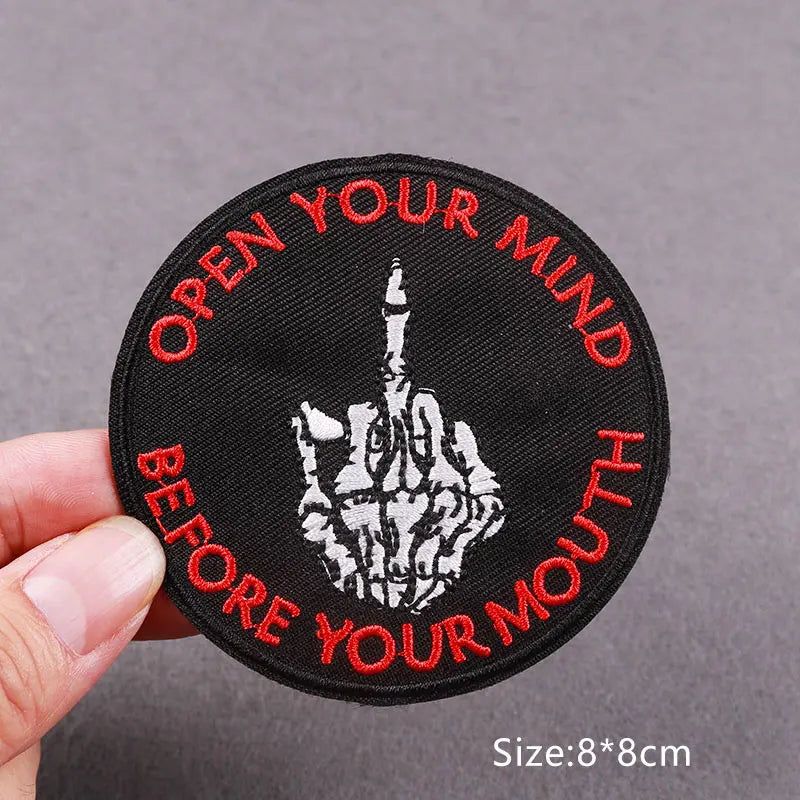 Black embroidered patch with red text Open Your Mind Before Your Mouth featuring a hand gesture