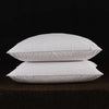 Two white natural goose down and feather sleeping pillows resting on a dark brown surface.