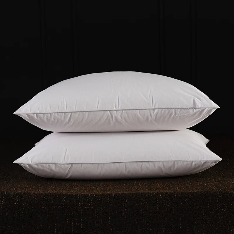 Two white natural goose down and feather sleeping pillows resting on a dark brown surface.