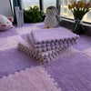 A purple plush interlocking puzzle rug mat is displayed on a purple rug with a stuffed penguin and flowers in the background.