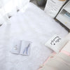 A white fluffy shag rug is displayed on a dark surface next to a book and a small pillow.