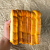 A hand holds a loaf of golden brown PU toast slices on a textured surface.