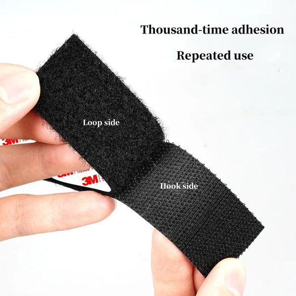 A hand holds a piece of black hook and loop tape showing the loop side and hook side for repeated use.