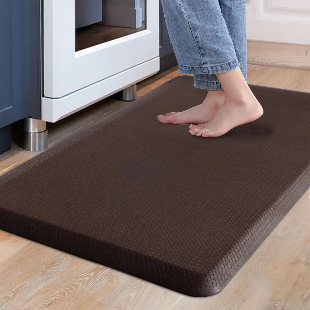 A brown anti-fatigue PVC kitchen mat is placed on a light wooden floor in front of a white appliance.