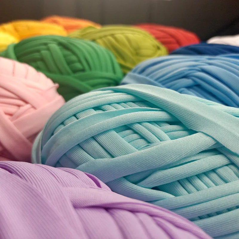 A close-up of various skeins of thick polyester craft yarn in shades of green, yellow, pink, and blue.