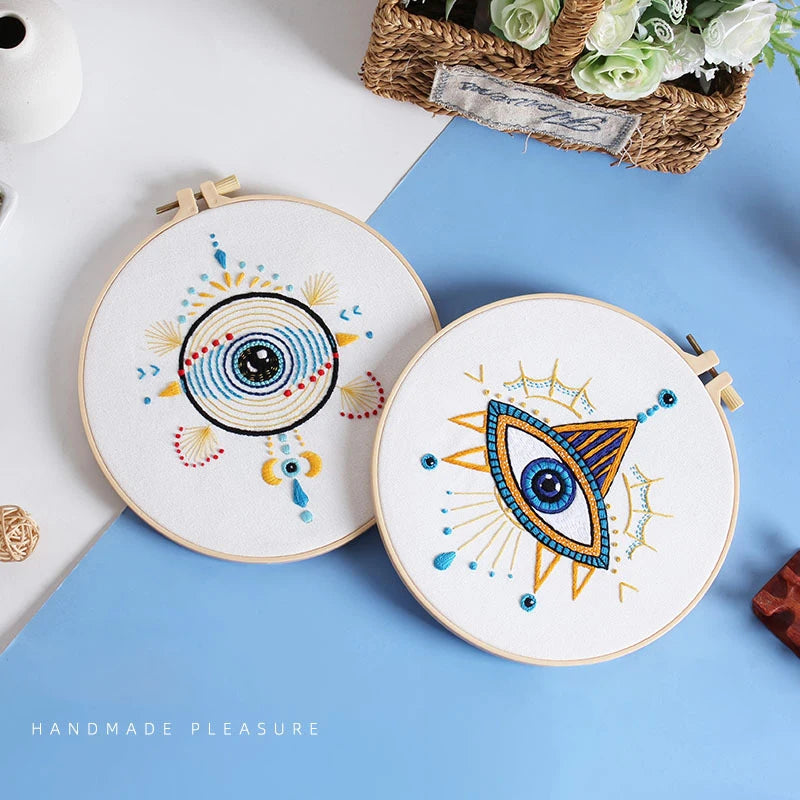 A round embroidery kit featuring a stylized eye design with star patterns on a white fabric against a blue background.