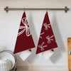 Two maroon kitchen towels with white bow designs hanging on a bar.