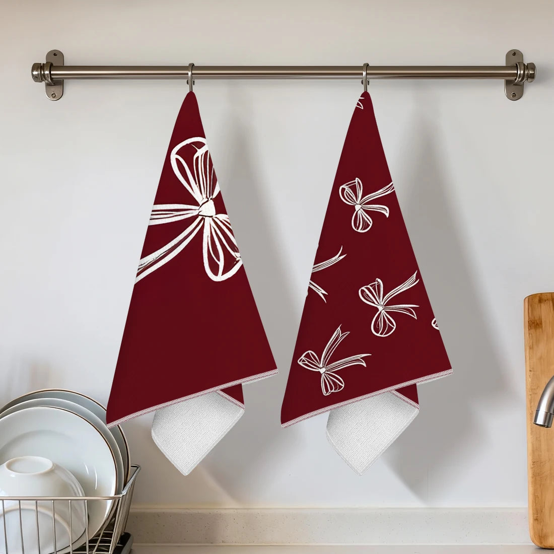 Two maroon kitchen towels with white bow designs hanging on a bar.