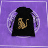 A black velvet pouch with a gold-colored silhouette of a cat on the front, set against a purple background.