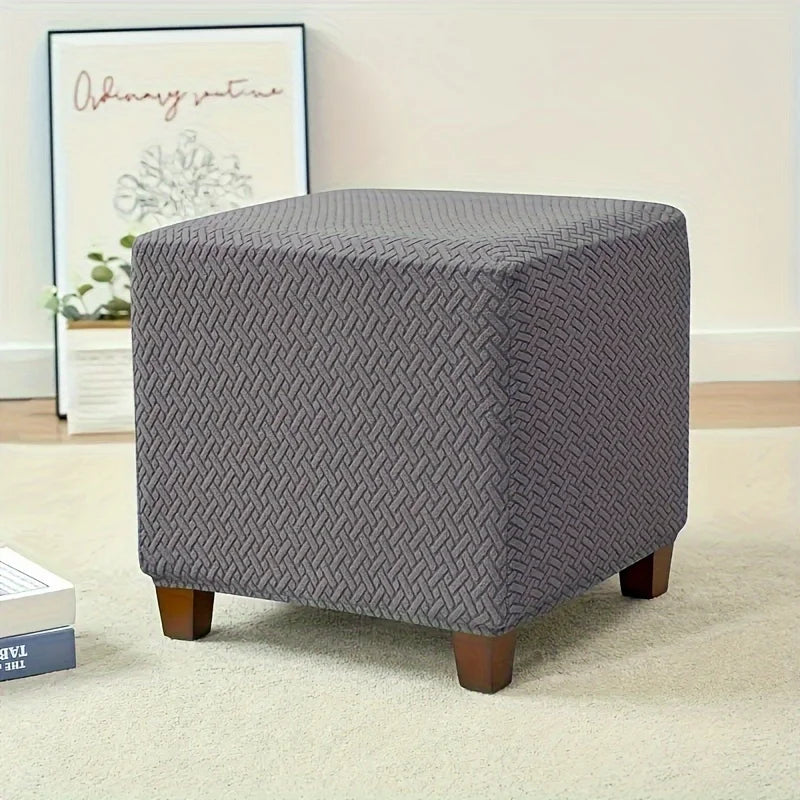 A gray woven fabric ottoman slipcover resting on a light carpet.