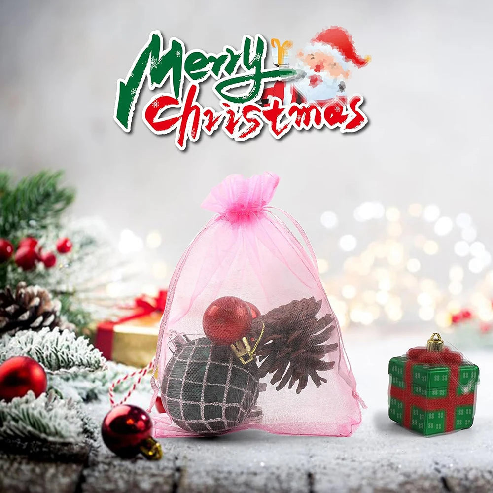 Pink organza gift bags filled with holiday decorations and jewelry on a rustic wooden surface.
