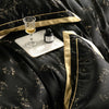 A luxury lyocell eucalyptus bedding set featuring black fabric with gold trim, a glass, and a small dark bottle on the bed.