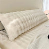 A fluffy, long, white plush pillow resting on a light-colored bed or surface.