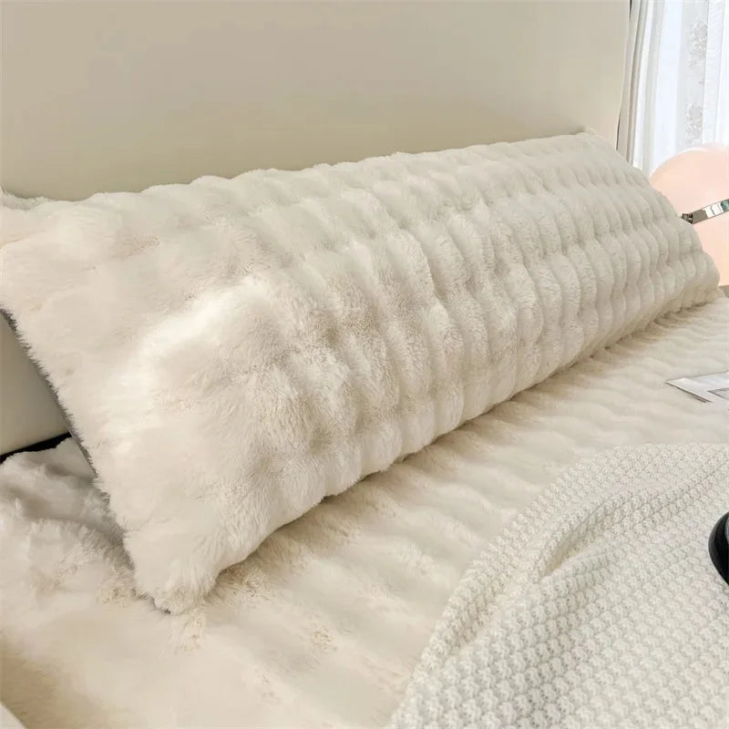 A fluffy, long, white plush pillow resting on a light-colored bed or surface.
