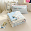 A stack of light blue and white quilted blankets and decorative pillows featuring cute bear designs.