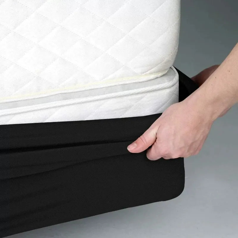 A hand is adjusting a black box spring protector cover over a white mattress.