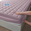 A hand is touching a quilted pink waterproof mattress protector on a bed.