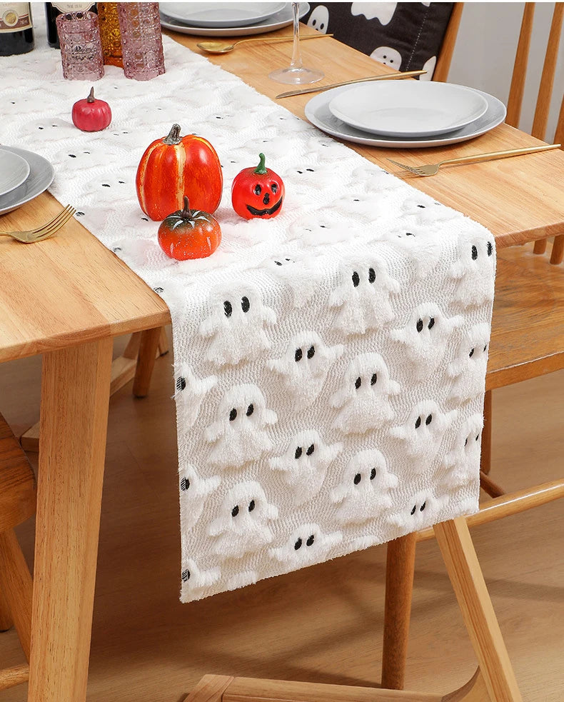 A white table runner with black ghost patterns is placed on a wooden table set for a festive occasion.