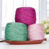 Three skeins of metallic silk yarn in shades of magenta, teal, and pink resting on a wooden tray.