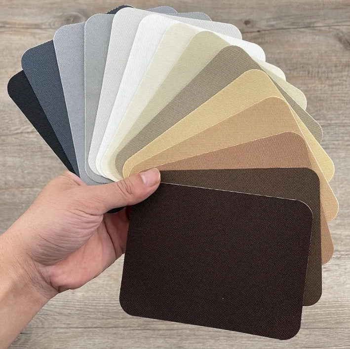 A hand holds a set of iron-on fabric repair patches in various shades of gray and beige.