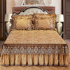 A luxurious bed set featuring a gold patterned bed skirt, matching pillowcases, and an ornate upholstered headboard.