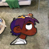 A plush cartoon character rug featuring a purple-haired figure with orange hair and yellow clothing on a gray carpet.