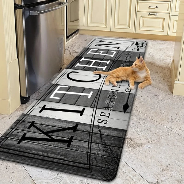 A long, rectangular kitchen mat with black and white text and a cat lying on it, placed on a light-colored floor.