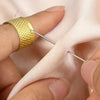 A hand is using a gold textured sewing needle to thread fabric, demonstrating a portable sewing needle kit for crafting.