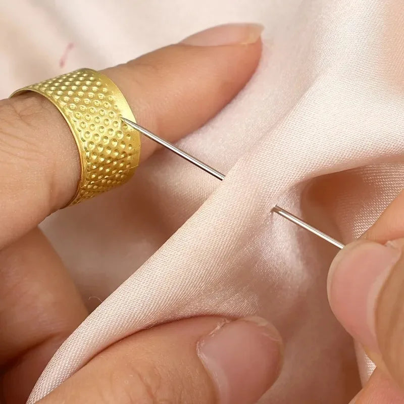 A hand is using a gold textured sewing needle to thread fabric, demonstrating a portable sewing needle kit for crafting.
