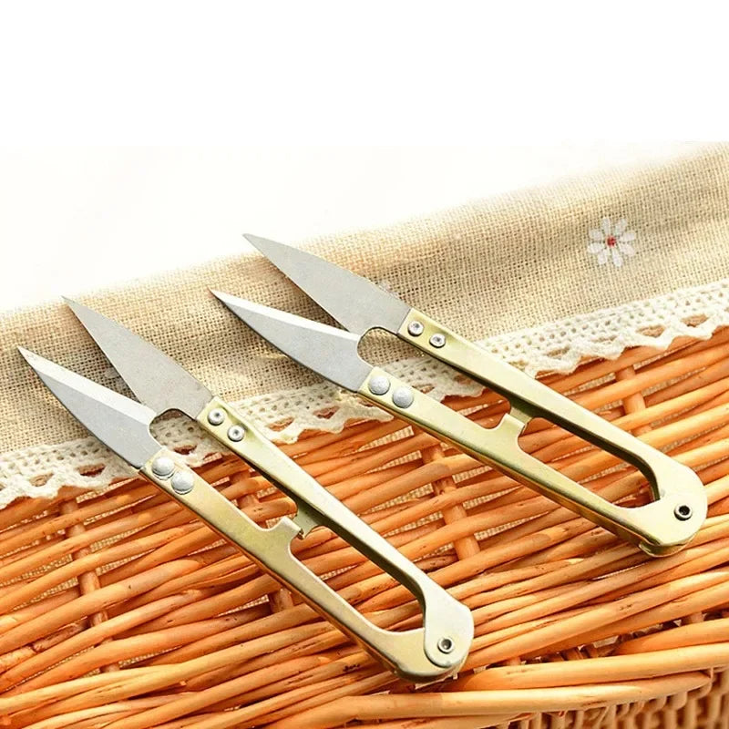 A pair of gold-toned U-shape sewing scissors resting on a woven straw mat.