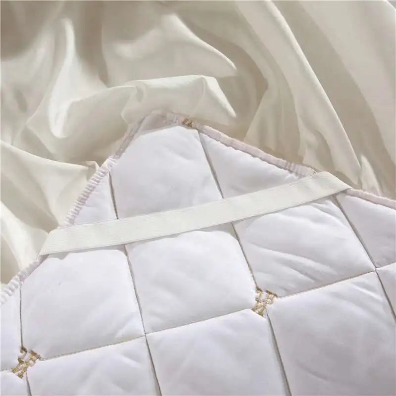 White quilted bed skirt with embroidered details draped over a white mattress.