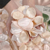 A hand holds a cluster of light pink silk rose petals for weddings and events.