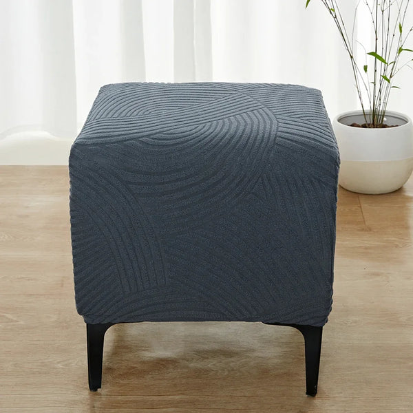 A dark blue geometric jacquard ottoman slipcover sitting on a wooden floor.